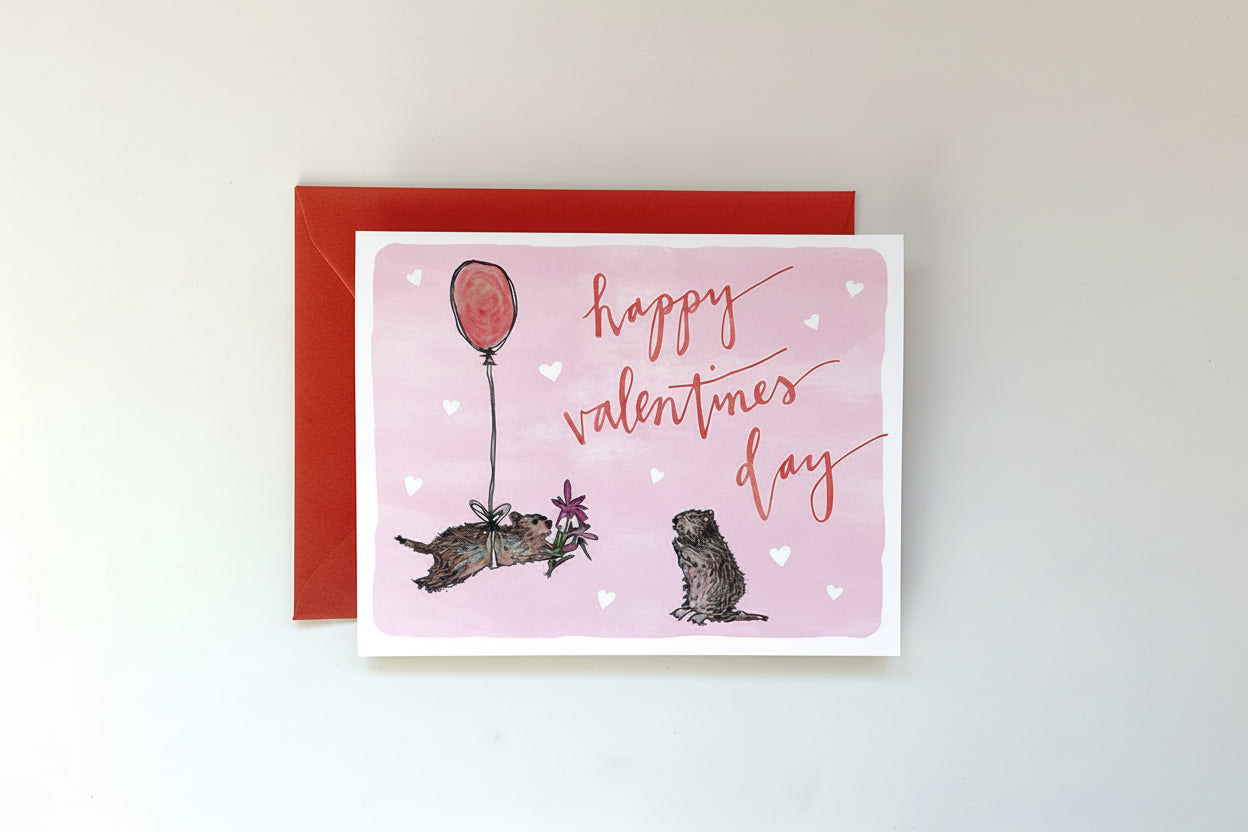 Valentine's Day card with two animals holding a balloon and 'Happy Valentine's Day' text on a pink background.