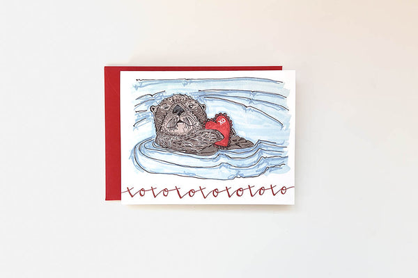 Card with illustration of an otter holding a heart, surrounded by water, on a white background.