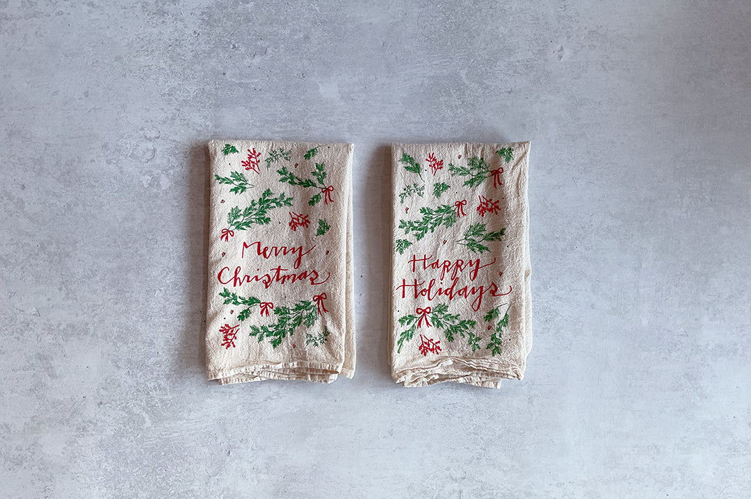 Two holiday-themed napkins with 'Merry Christmas' and 'Happy Holidays' text on a gray background.
