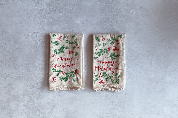 Two holiday-themed napkins with 'Merry Christmas' and 'Happy Holidays' text on a gray background.